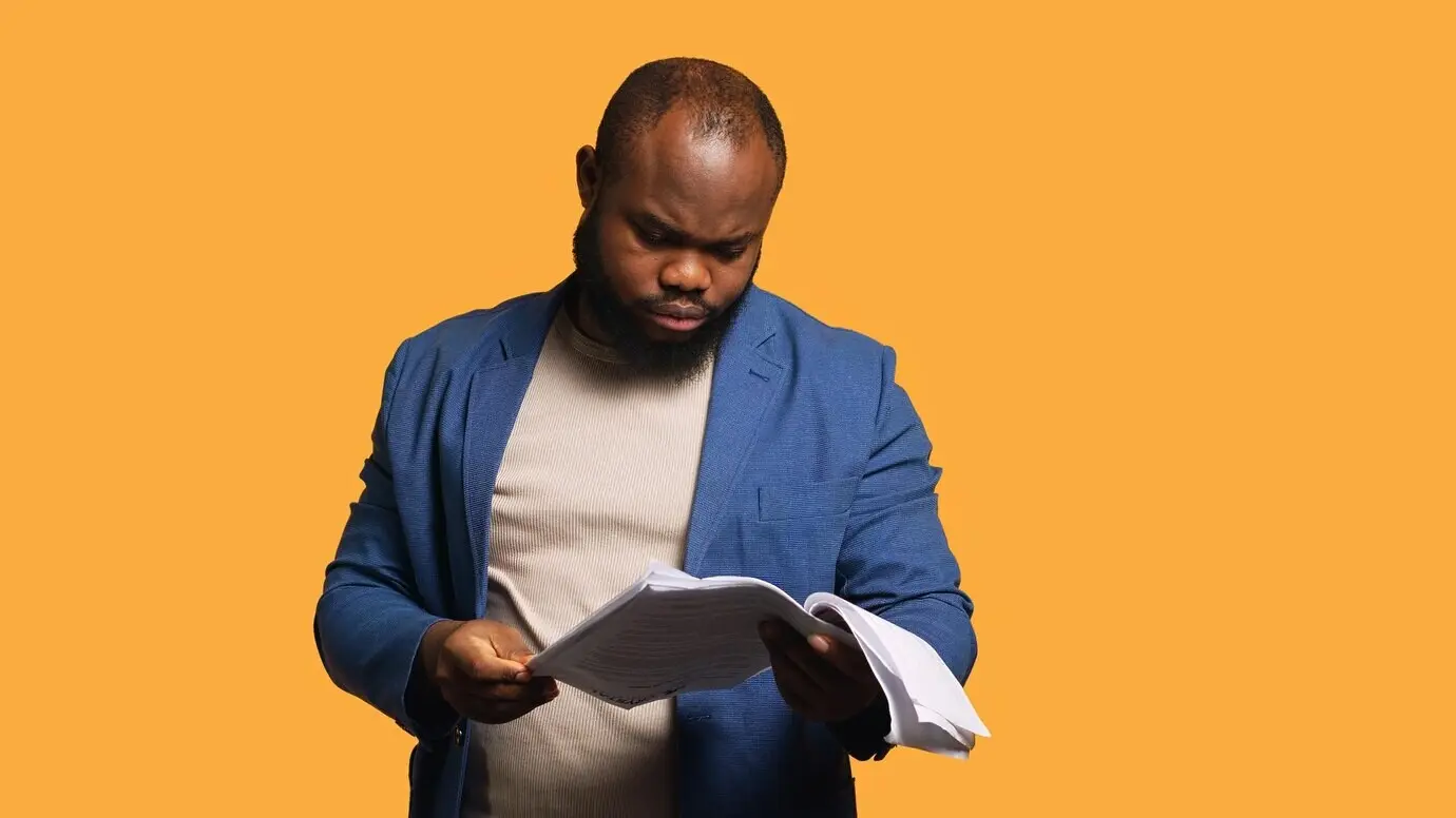 Ein Mann blättert in Berichtsunterlagen, wirft sie wütend weg und fühlt sich überarbeitet.